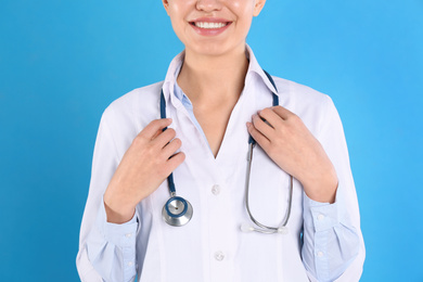 Photo of Young doctor with stethoscope on blue background, closeup