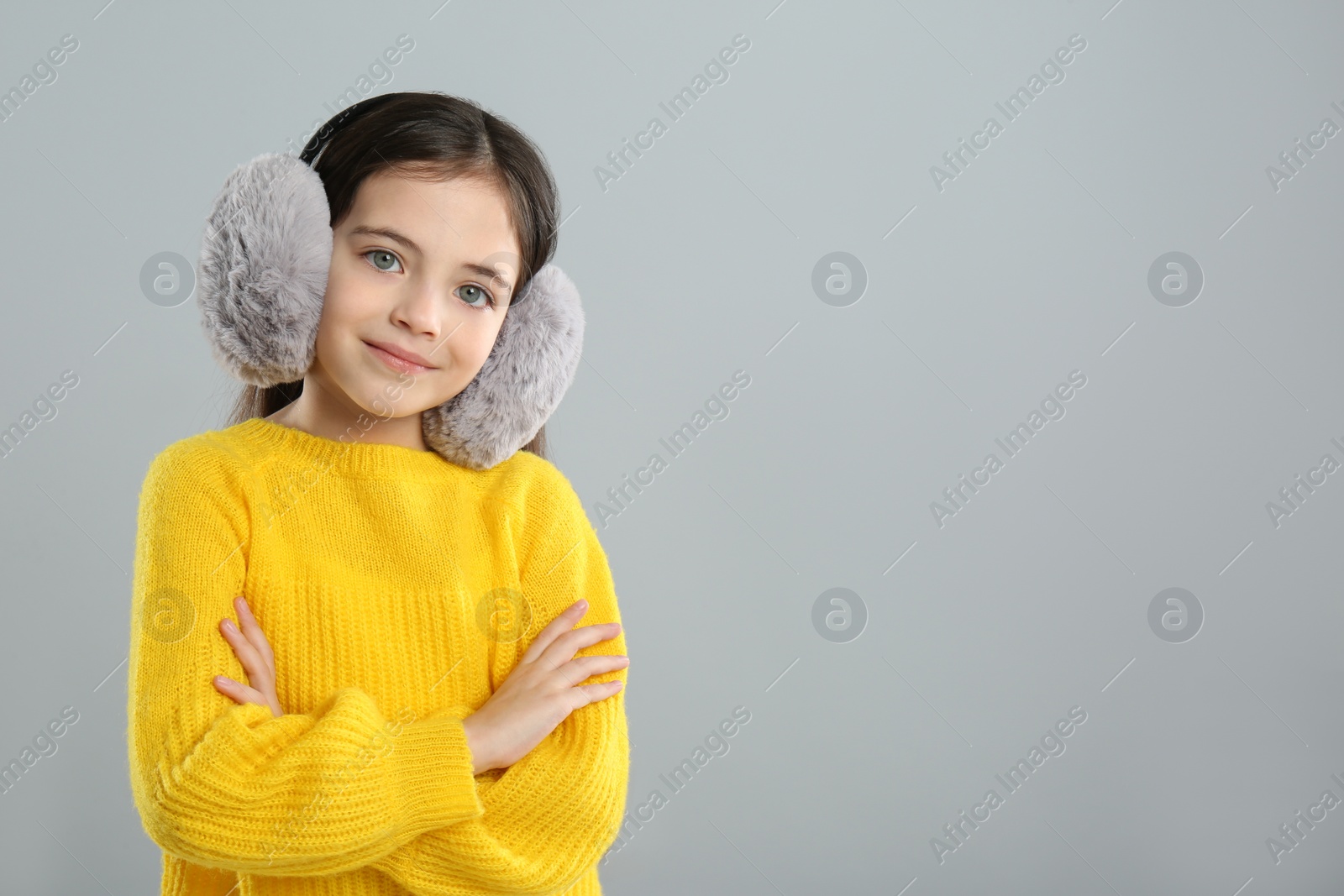 Photo of Cute girl wearing stylish earmuffs on grey background. Space for text