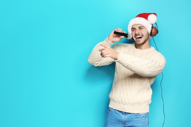 Photo of Young man in Santa hat singing into microphone on color background. Christmas music