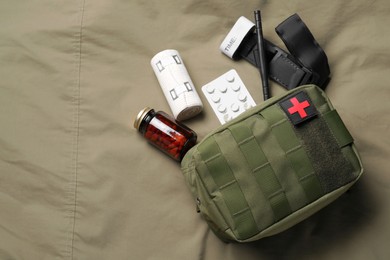 Photo of Military first aid kit, tourniquet, pills and elastic bandage on khaki fabric, flat lay. Space for text