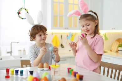 Easter celebration. Cute children with bunny ears painting eggs at white marble table in kitchen