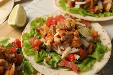 Delicious tacos with vegetables, meat and lime on table, closeup