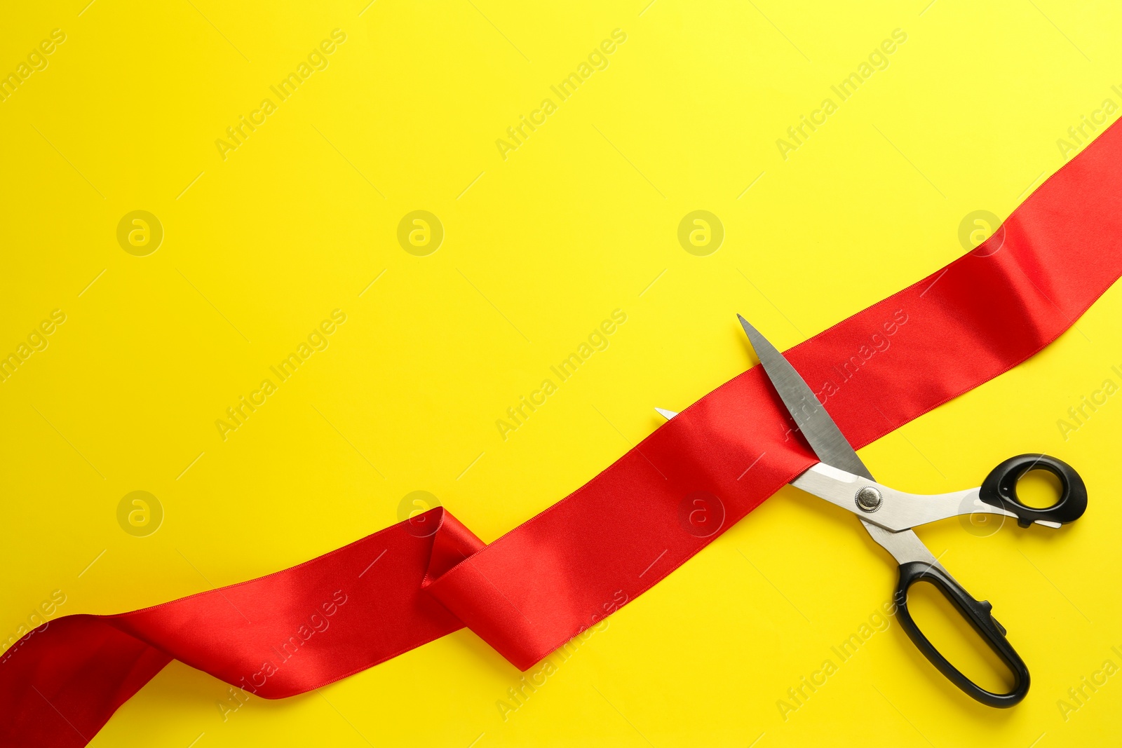 Photo of Red ribbon and scissors on yellow background, top view. Space for text