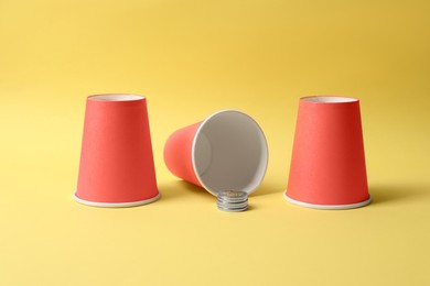 Photo of Three red cups and coins on yellow background. Thimblerig game