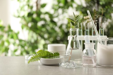 Photo of Natural ingredients for cosmetic products and laboratory glassware on grey table against blurred green background