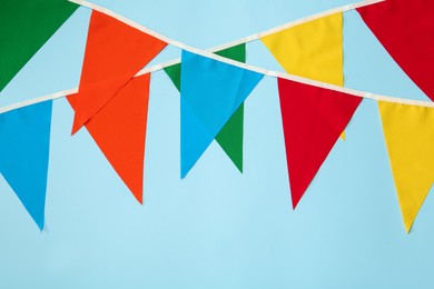 Photo of Buntings with colorful triangular flags on light blue background. Festive decor