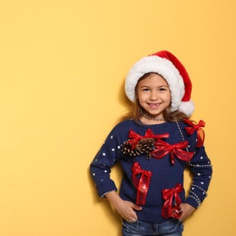 Photo of Cute little girl in handmade Christmas sweater on color background. Space for text
