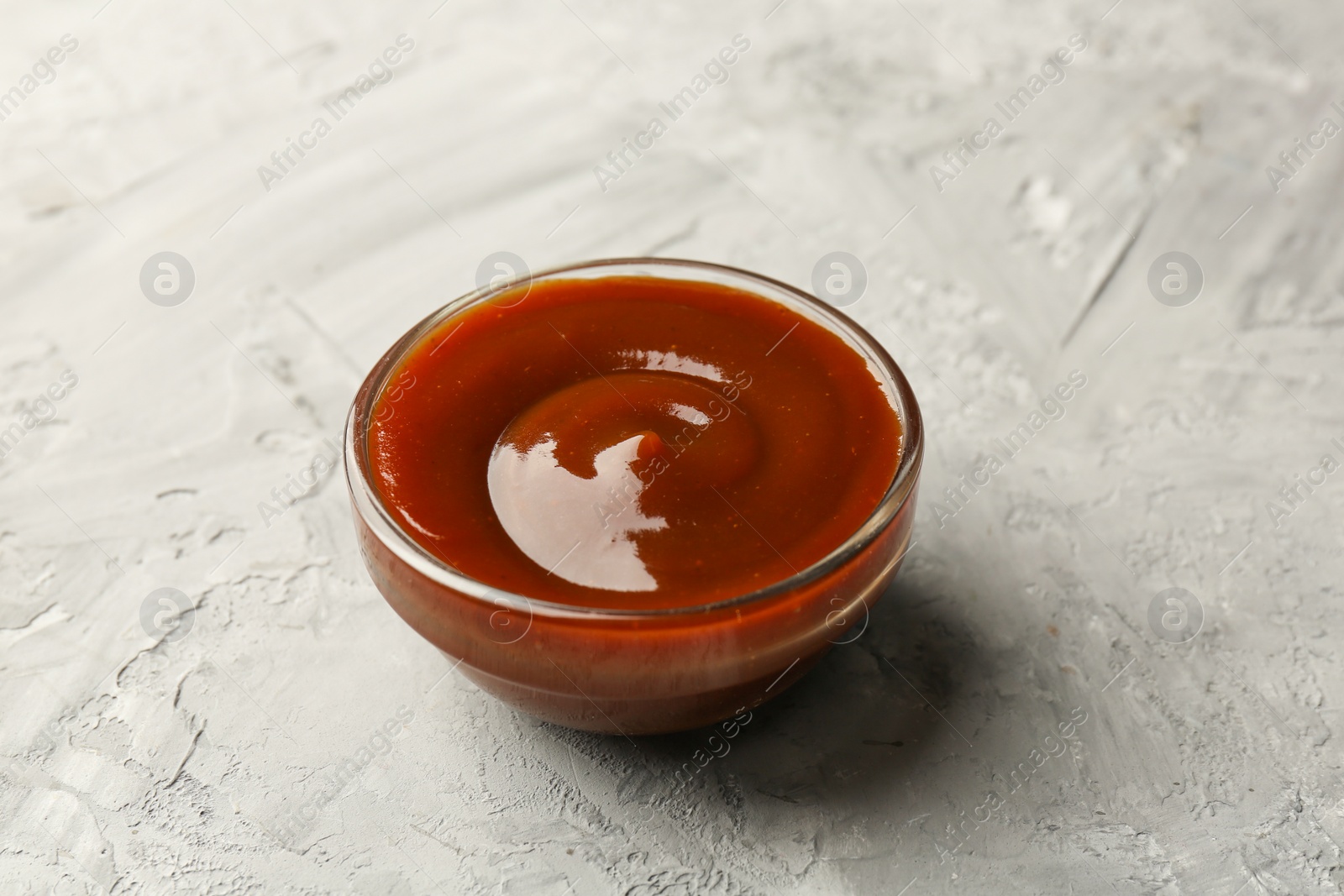 Photo of Tasty barbeque sauce in bowl on grey textured table, closeup