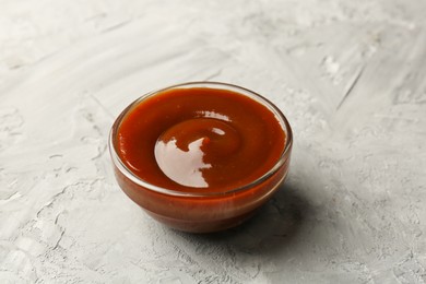 Tasty barbeque sauce in bowl on grey textured table, closeup