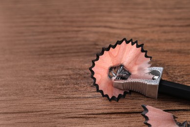 Photo of Metal sharpener with pencil shavings on wooden table, closeup. Space for text