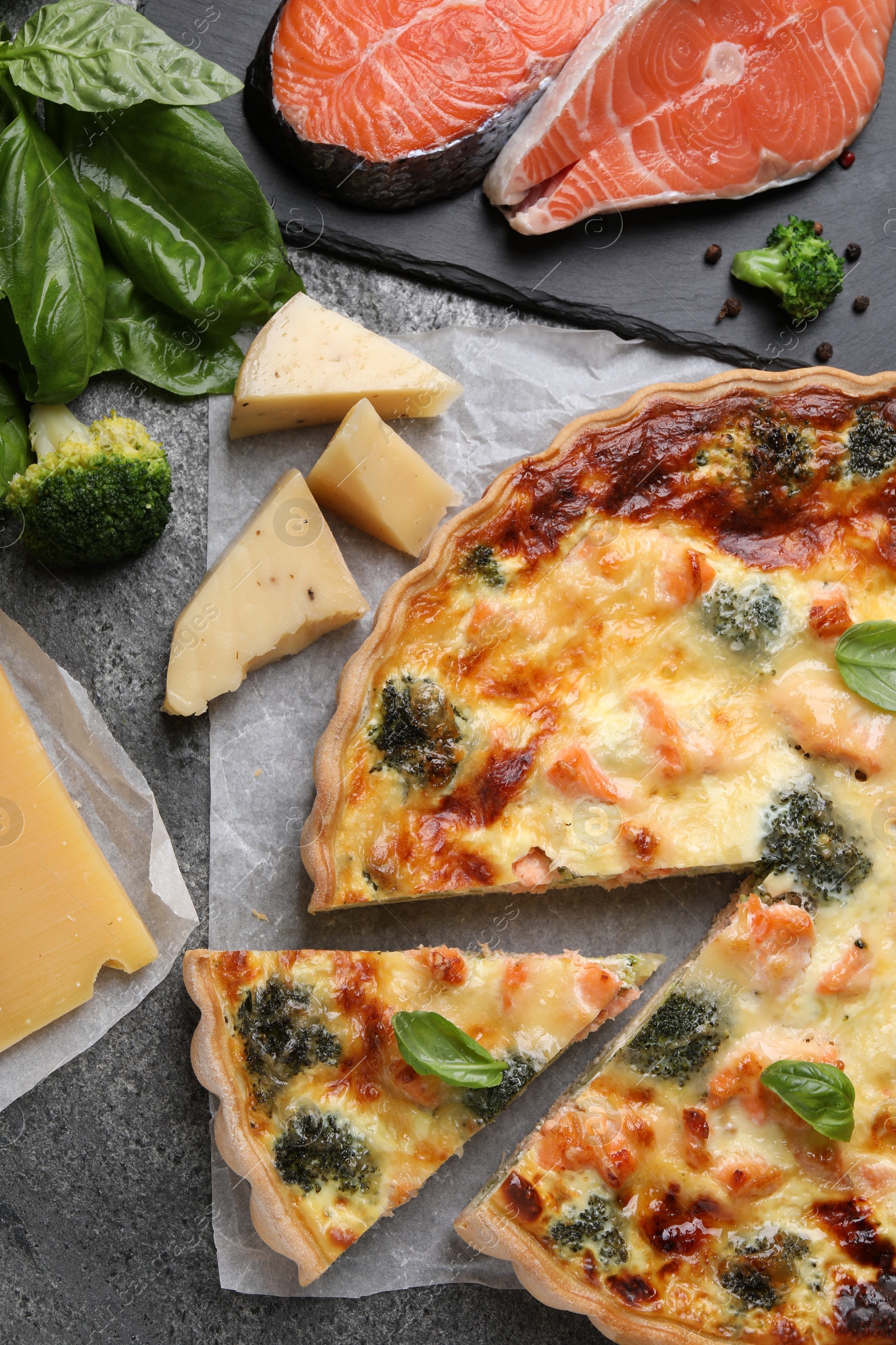 Photo of Delicious homemade quiche and ingredients on gray table, flat lay