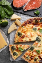 Delicious homemade quiche and ingredients on gray table, flat lay