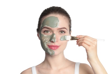 Photo of Young woman applying clay mask on her face against white background. Skin care