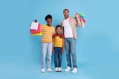 Photo of Family shopping. Happy parents and son with colorful bags on light blue background