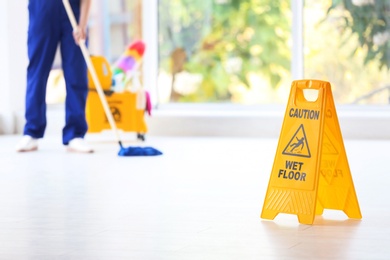 Photo of Safety sign with phrase Caution wet floor and blurred cleaner on background