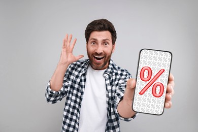 Image of Discount, offer, sale. Emotional man showing mobile phone with percent signs on screen, grey background