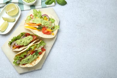 Photo of Delicious tacos with guacamole, meat and vegetables on light grey table, flat lay. Space for text