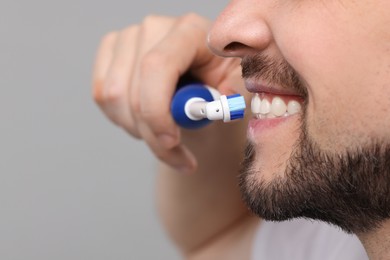 Photo of Man brushing his teeth with electric toothbrush on light grey background, closeup. Space for text