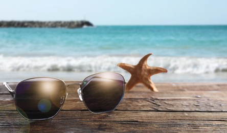 Image of Starfish and stylish sunglasses on wooden table near sea 