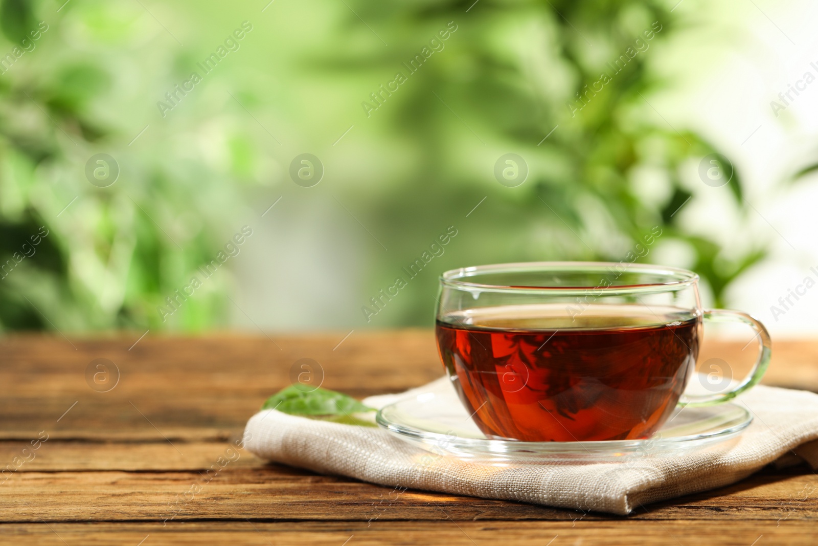 Photo of Cup of black tea on wooden table against blurred background. Space for text