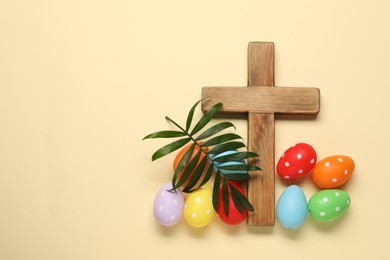 Photo of Wooden cross, painted Easter eggs and palm leaf on beige background, flat lay. Space for text