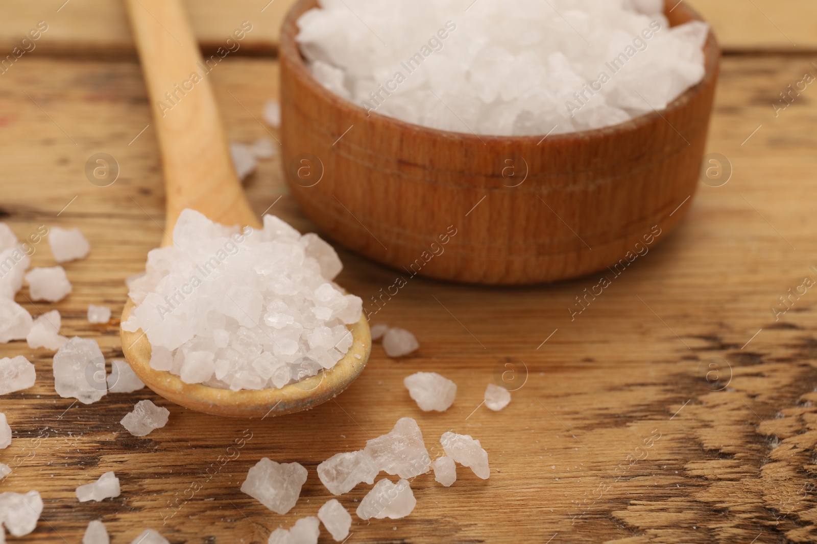 Photo of Bowl and spoon with sea salt on wooden table, closeup