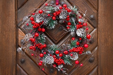 Beautiful Christmas wreath with berries and cones hanging on wooden door