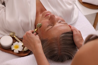 Photo of Woman receiving facial massage with jade roller in beauty salon, closeup