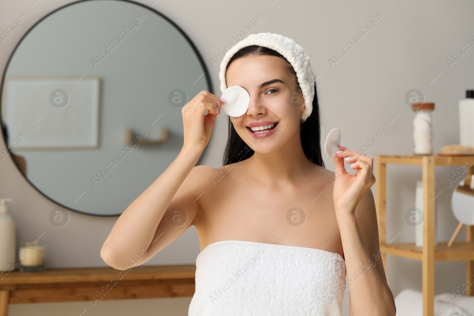 Photo of Young woman using cotton pad with micellar water indoors