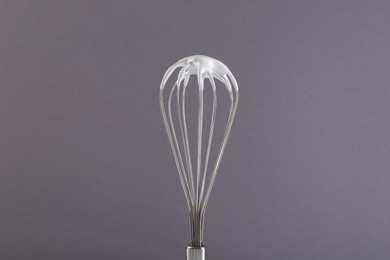 Photo of Whisk with whipped cream on grey background