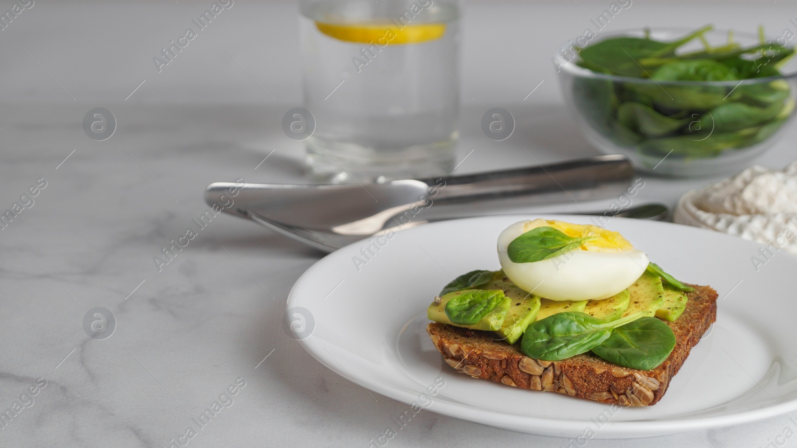 Photo of Tasty sandwich with boiled egg, avocado and spinach on white marble table, space for text