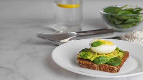 Photo of Tasty sandwich with boiled egg, avocado and spinach on white marble table, space for text