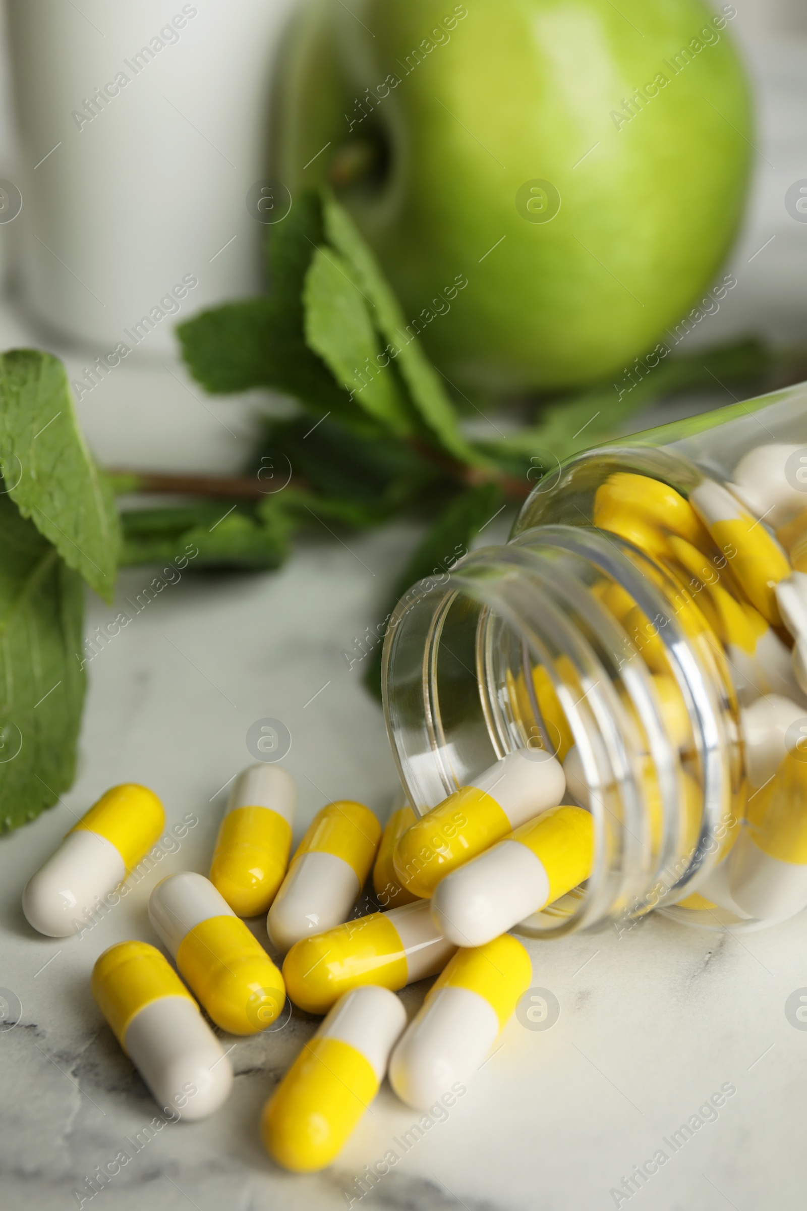 Photo of Bottle with vitamin pills, apples and mint on white marble table, closeup