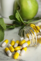 Bottle with vitamin pills, apples and mint on white marble table, closeup