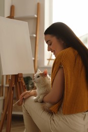 Photo of Beautiful young woman with drawing brush and cat at home