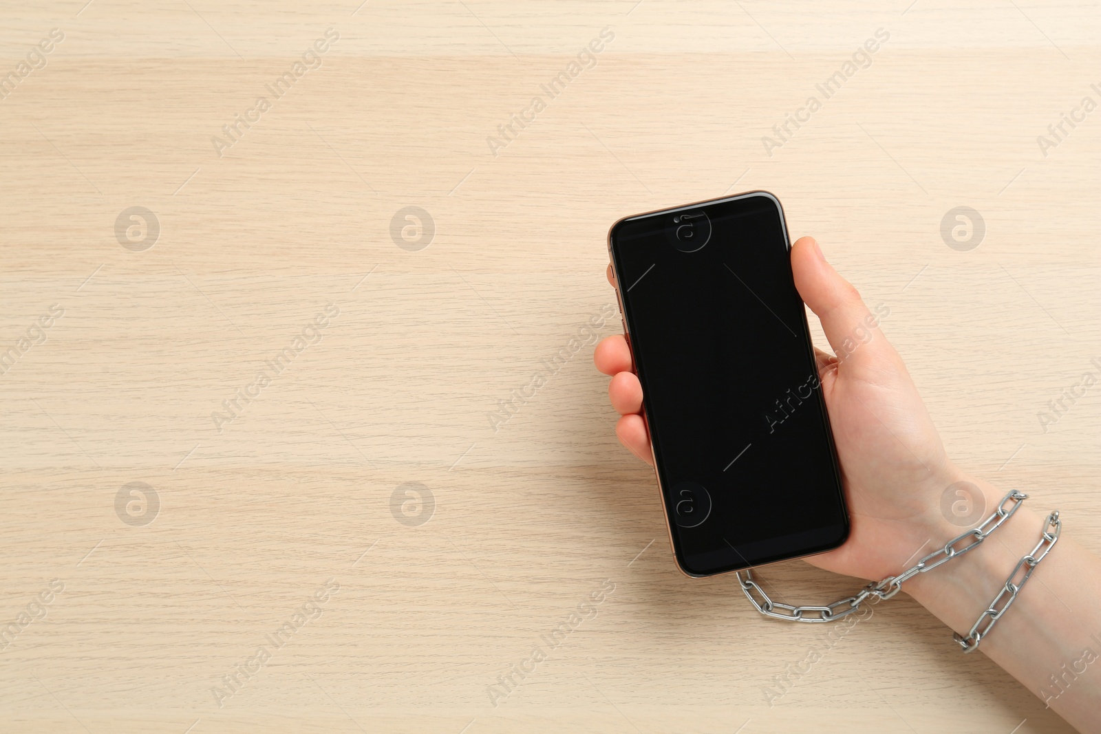 Photo of Internet addiction. Top view of woman holding smartphone at wooden table, hand chained to device