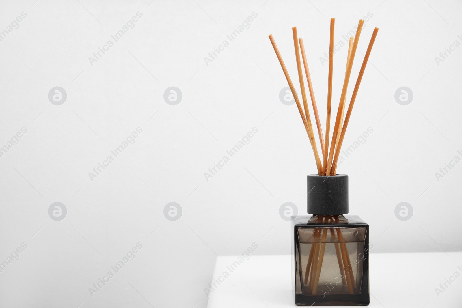 Photo of Aromatic reed freshener on table near white wall, space for text