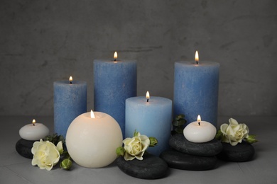 Burning candles, spa stones and flowers on grey table