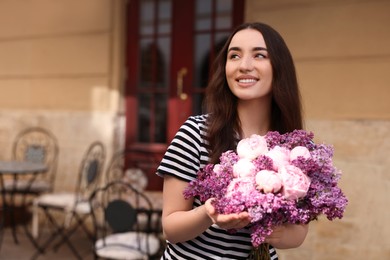 Beautiful woman with bouquet of spring flowers on city street, space for text