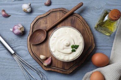 Tasty mayonnaise in bowl, ingredients and whisk on gray wooden table, flat lay