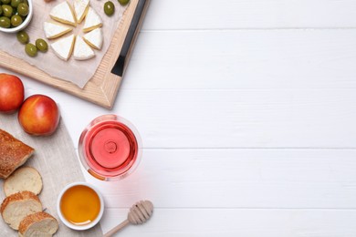 Photo of Glass of delicious rose wine and snacks on white wooden table, flat lay. Space for text
