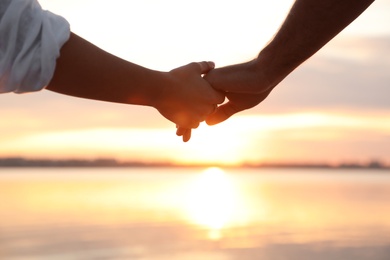 Photo of Man and woman holding hands together at sunset, closeup. Nature healing power