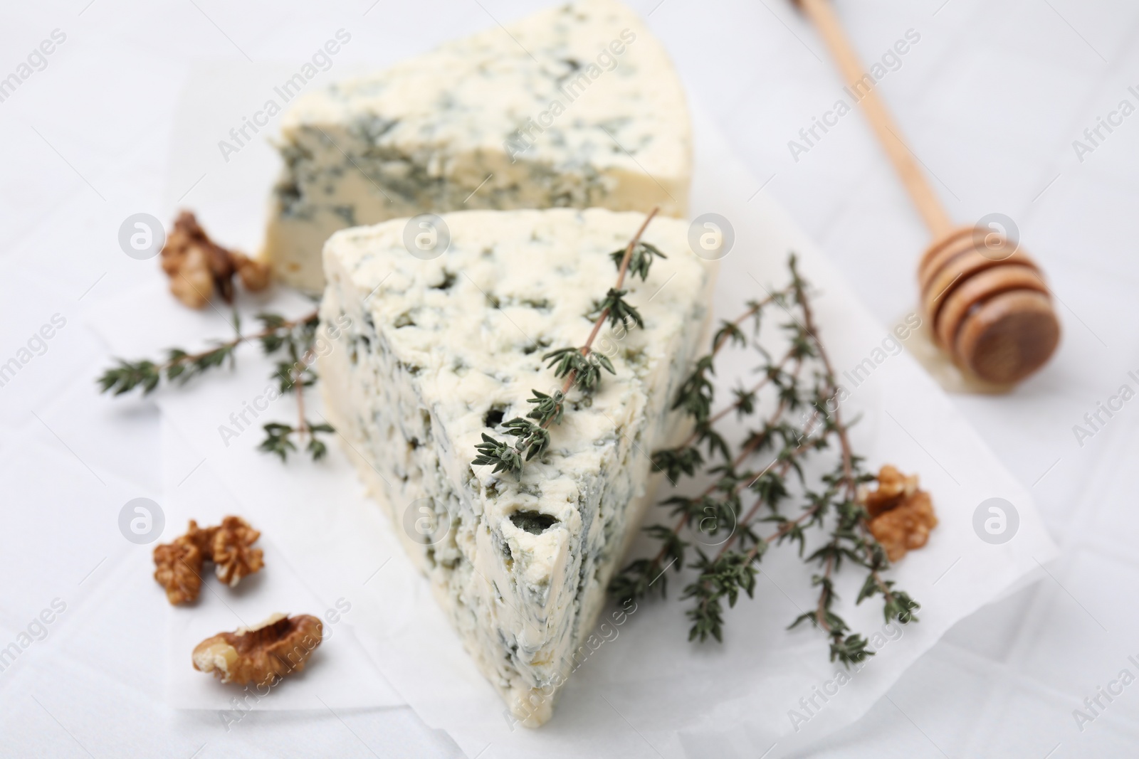 Photo of Tasty blue cheese with thyme, walnuts and honey dipper on white table, closeup