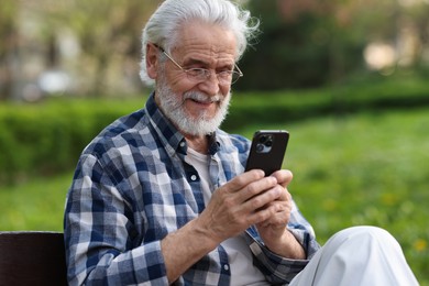 Portrait of happy grandpa with glasses using smartphone on bench in park