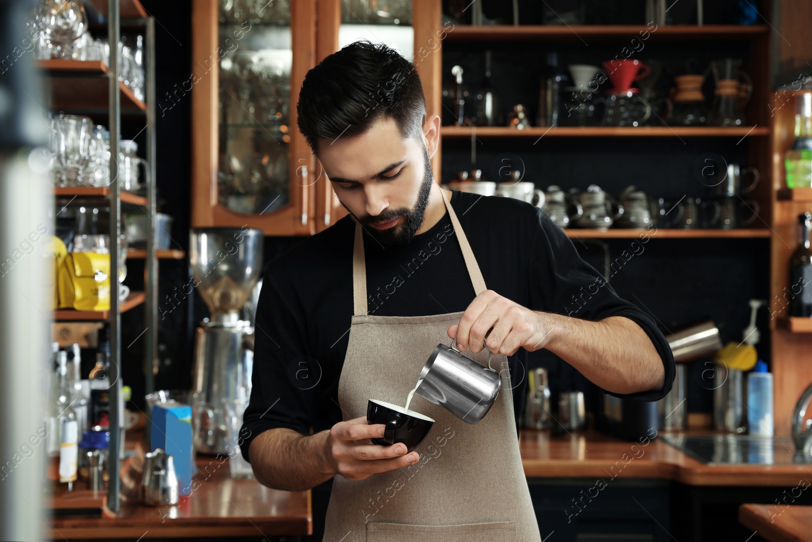 Photo of Portrait of barista pouring milk into cup of coffee against bar shelves in cafe