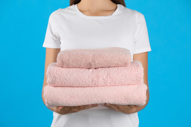 Woman holding fresh towels on light blue background, closeup