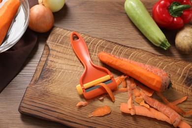 Peels, peeler and fresh vegetables on wooden table, flat lay