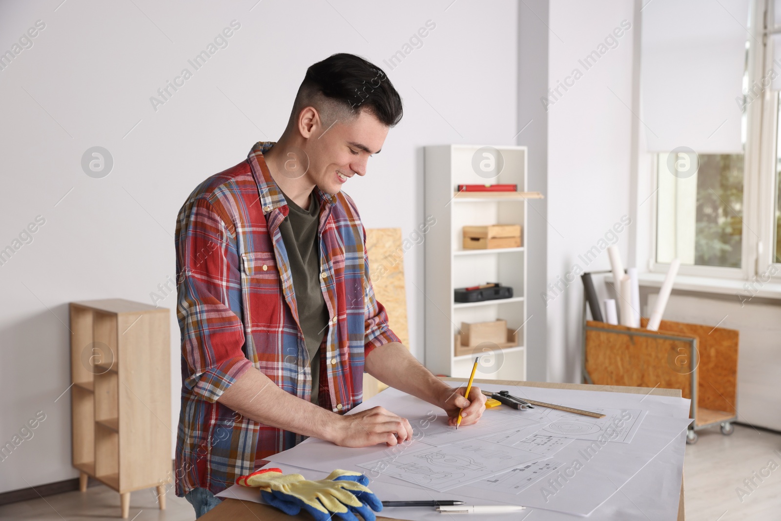 Photo of Young handyman working with blueprints at table in room