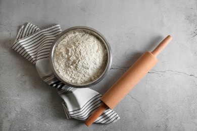 Photo of Flour in bowl, rolling pin and napkin on grey table, top view
