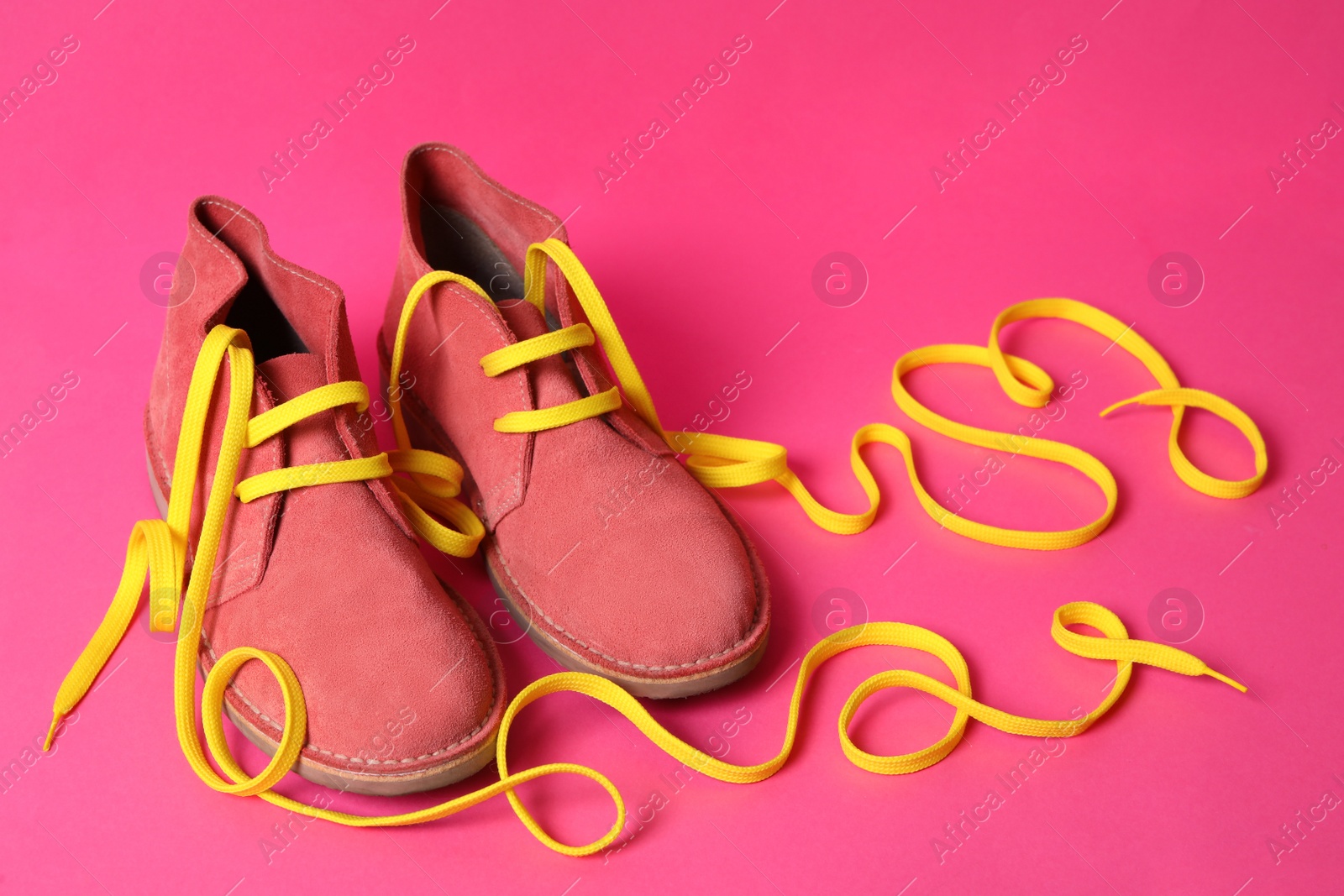 Photo of Stylish shoes with yellow laces on pink background